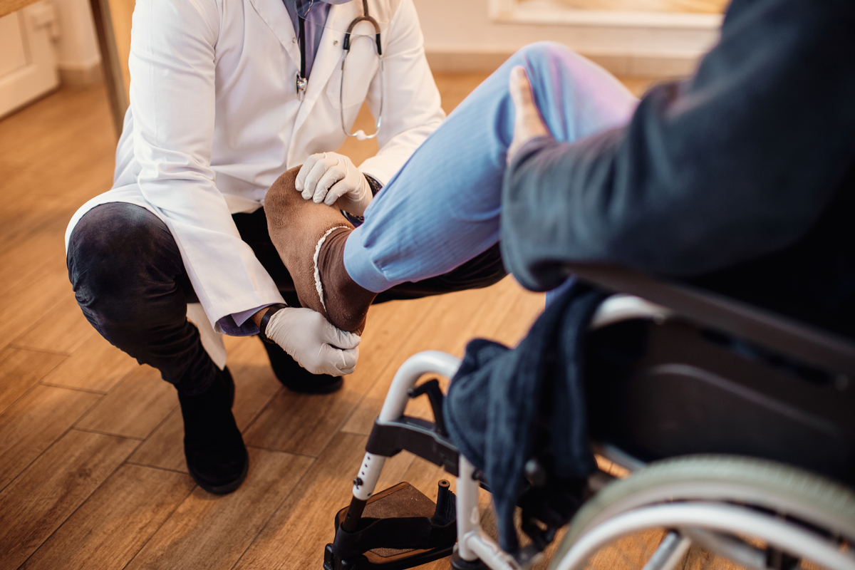 Unrecognizable senior man in wheelchair getting his leg examined by a doctor at nursing home.